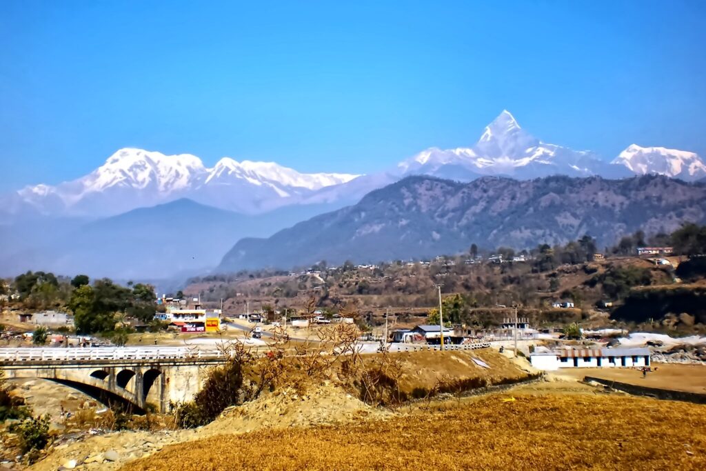 Snow-capped Himalayan peak above rural valley with bridge and settlement