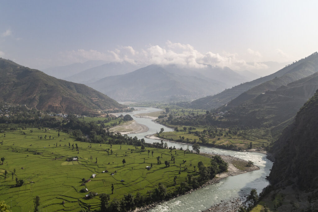 Winding river through green Himalayan valley with rice fields and mountains
